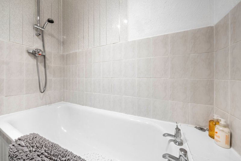 Clean bathroom with white bathtub, beige tile walls, shower head and bath accessories