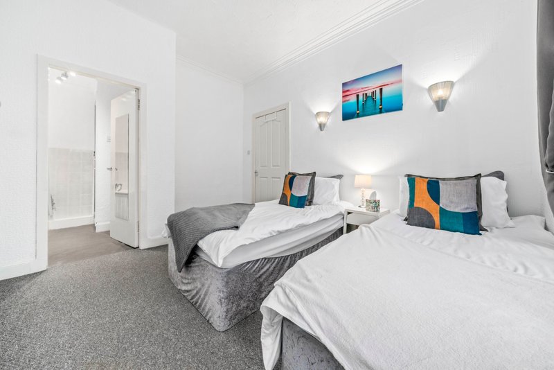 Bright bedroom with two single beds, white bedding, colorful cushions and wall art