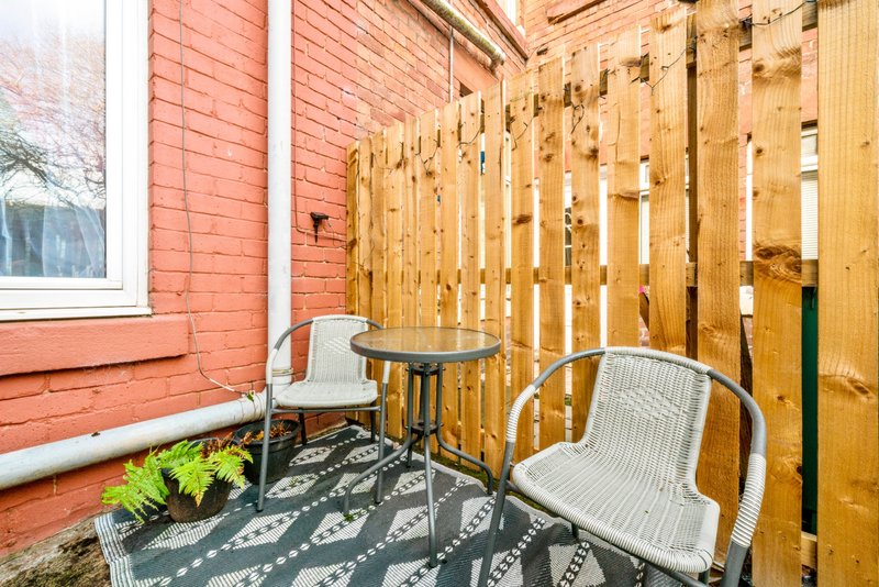Outdoor patio area with two wicker chairs, small table, wooden fence and red brick building