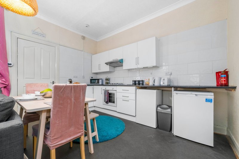 Kitchen with white cabinets, dining table, chair with towel, and appliances