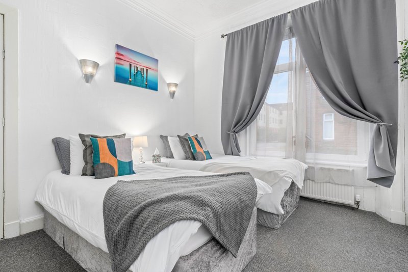 Bright bedroom with twin beds, colorful pillows, grey curtains and wall art