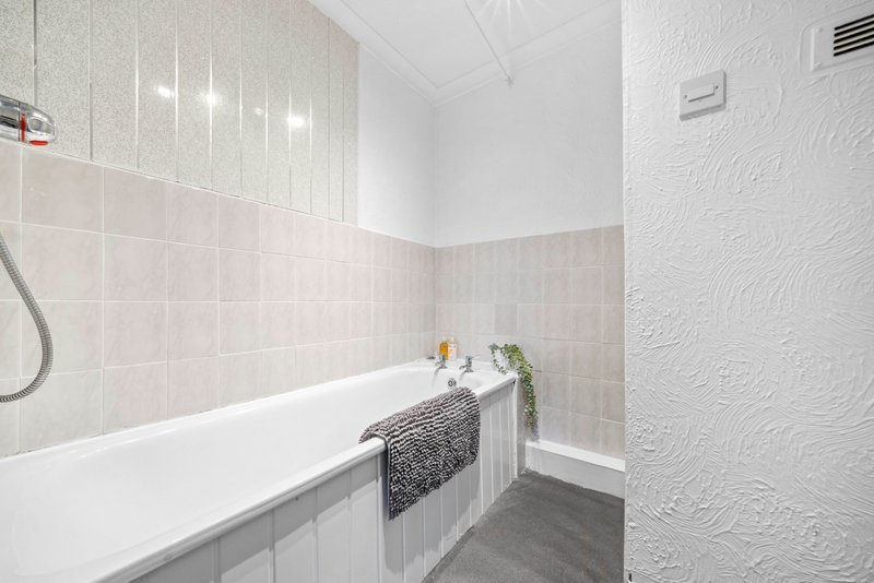 Modern bathroom with white bathtub, pink tile walls, towel rail and mirrored cabinet
