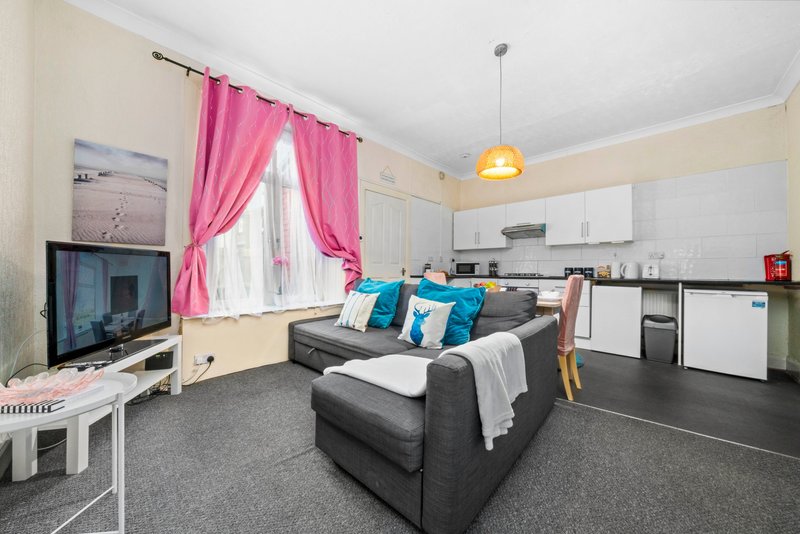 Open-plan living room and kitchen with grey sofa, pink curtains, TV, and white cabinetry