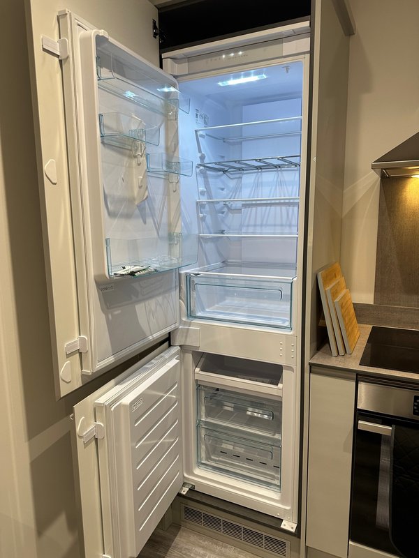 Open white refrigerator with freezer compartment below, empty shelves visible inside