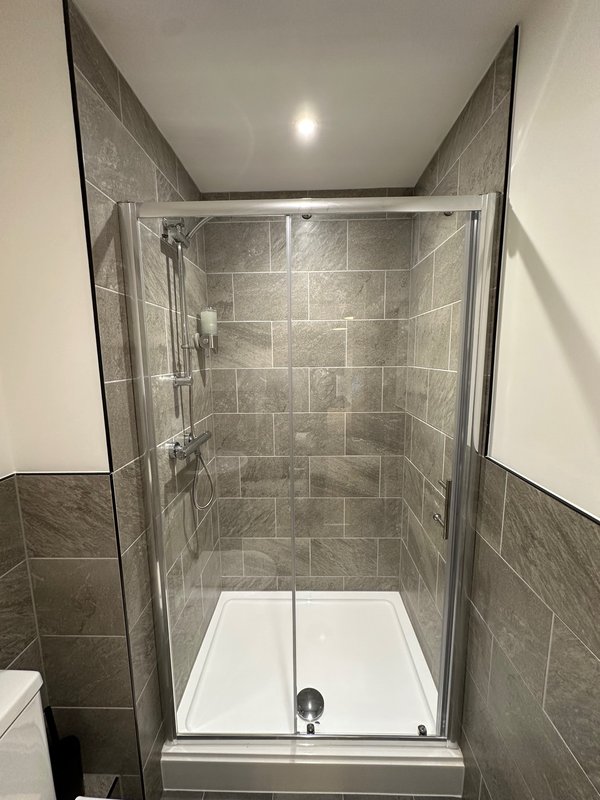 Modern bathroom with grey tile shower enclosure, white tray, and recessed lighting