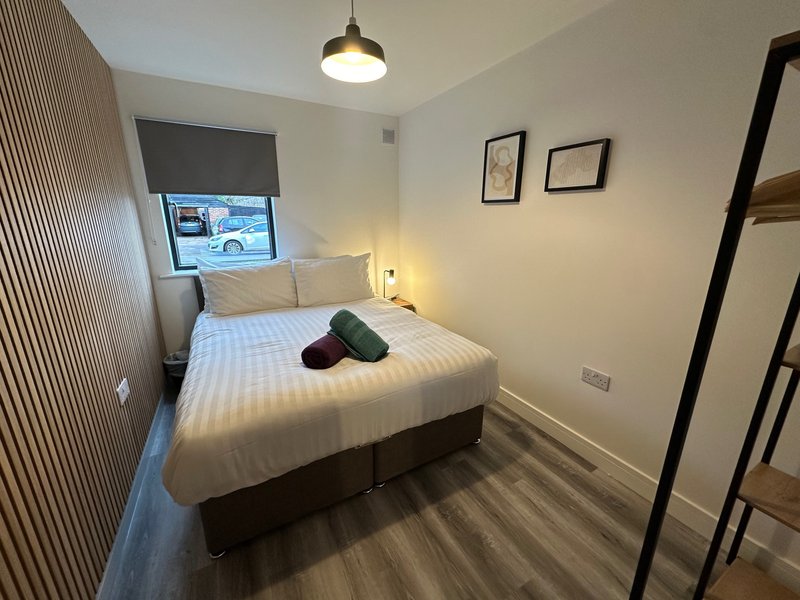 Small bedroom with double bed, pendant light, striped rug and window with blind