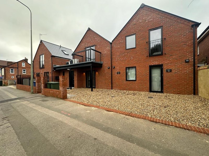 Modern brick residential building with gravel driveway, green doors and street frontage