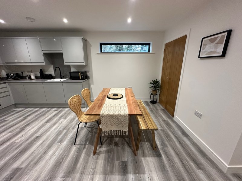 Open-plan kitchen and dining area with wooden table, chairs, striped flooring and white cabinetry