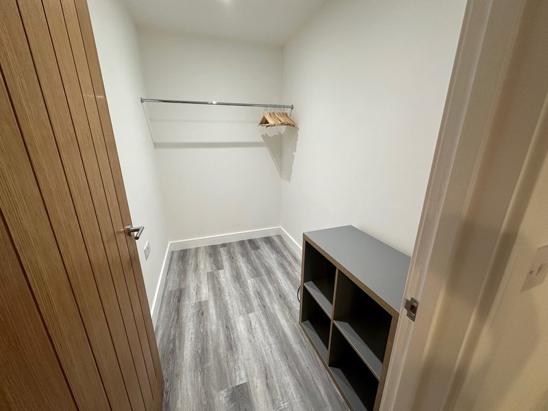 Small walk-in closet with wooden sliding door, shelving, storage cubbies and vinyl flooring