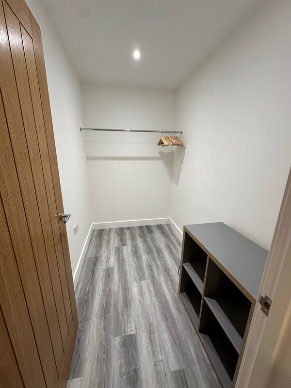 Narrow hallway with gray vinyl flooring, white walls, wooden door, and black storage shelves