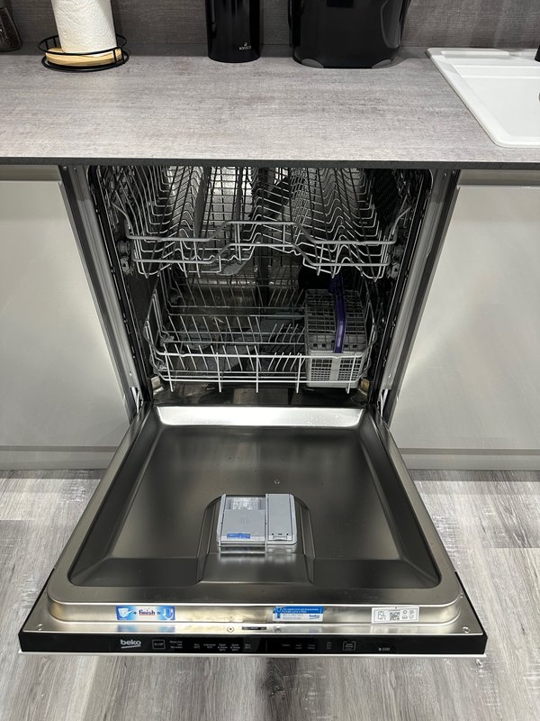 Open dishwasher with stainless steel interior, granite countertop, and kitchen appliances above