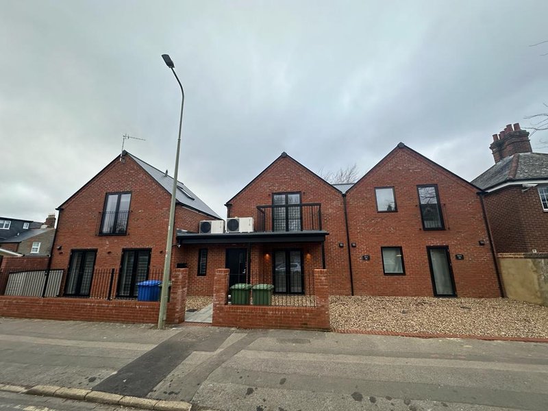 Modern brick residential building with multiple gabled roofs, gravel driveway, and street frontage
