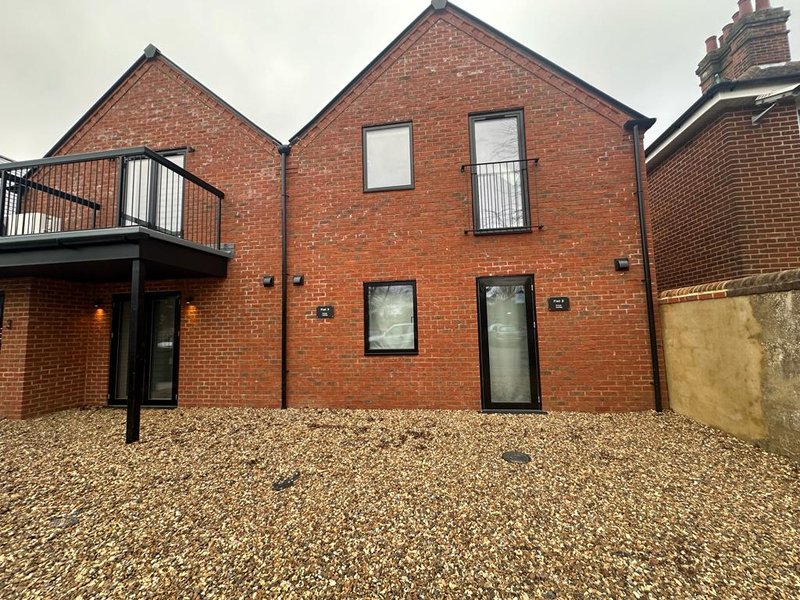Modern brick house exterior with gravel driveway, metal balcony and contemporary black-framed doors and windows
