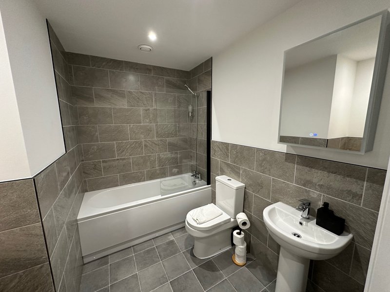 Modern bathroom with bathtub, toilet, pedestal sink, mirror and grey tile walls