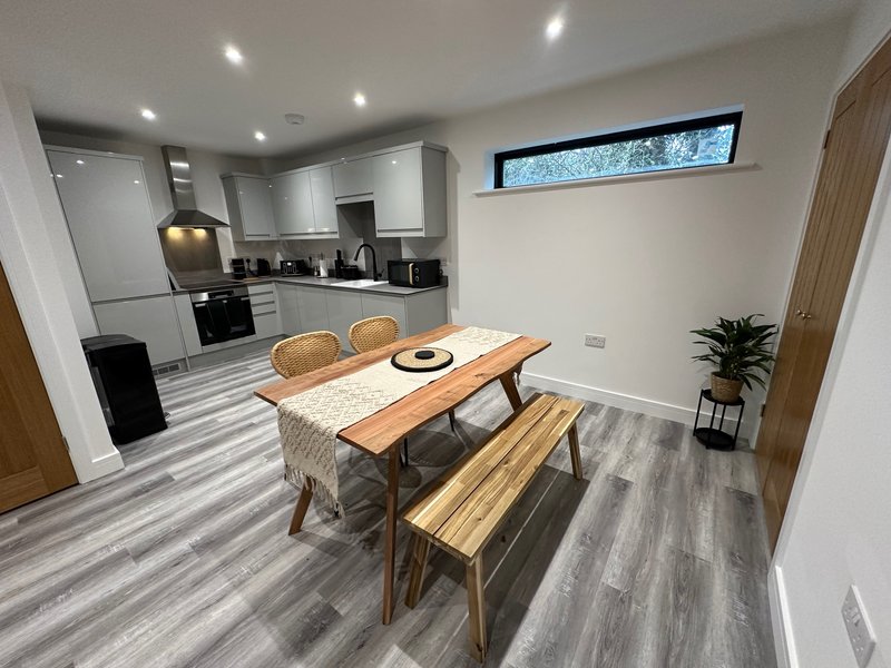 Open-plan kitchen and dining area with wood table, modern cabinetry, and high window