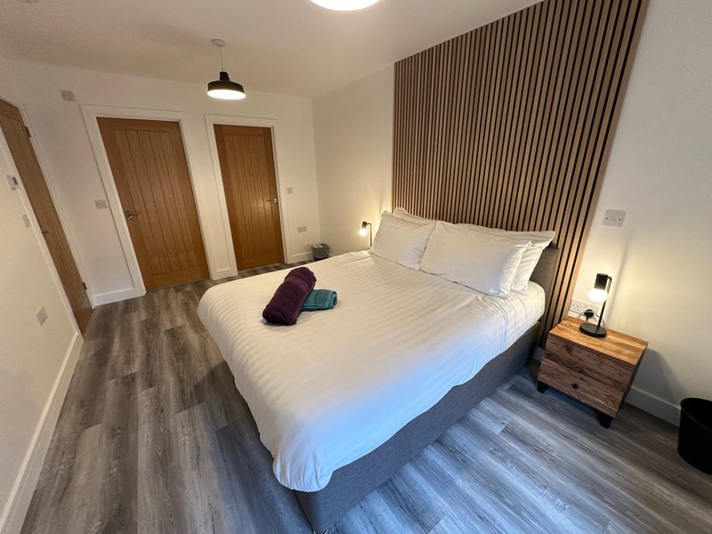 Modern bedroom with double bed, white bedding, wooden doors, and vertical wall paneling