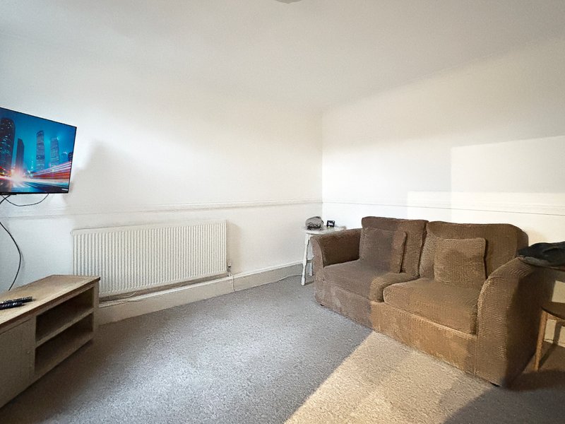 Living room with brown sofa, wall-mounted TV, radiator and light carpeting