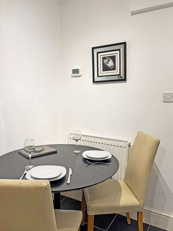 Dining area with round black table, two beige chairs, place settings, and framed wall art
