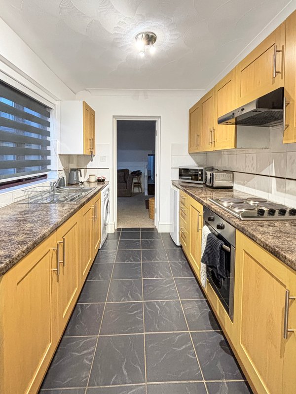 Modern galley kitchen with yellow cabinetry, granite countertops, stainless steel appliances and dark tile flooring