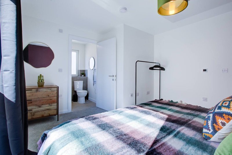 Modern bedroom with double bed, wooden dresser, ensuite bathroom visible, and pendant lighting