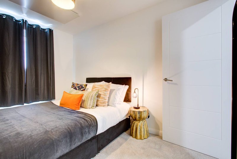 Modern bedroom with double bed, orange accent pillow, gold side table and white wardrobe