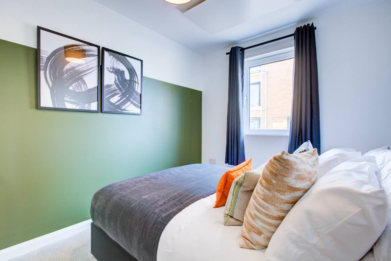 Modern bedroom with double bed, green accent wall, framed artwork, and blue curtains