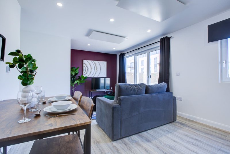 Open-plan living and dining area with blue sofa, wooden dining table, plants and windows