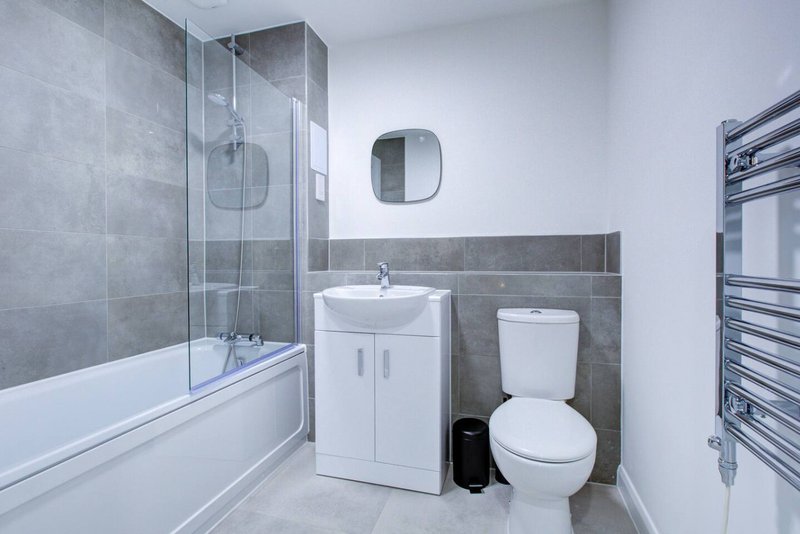 Modern bathroom with gray tile walls, white sink vanity, toilet, and glass shower enclosure