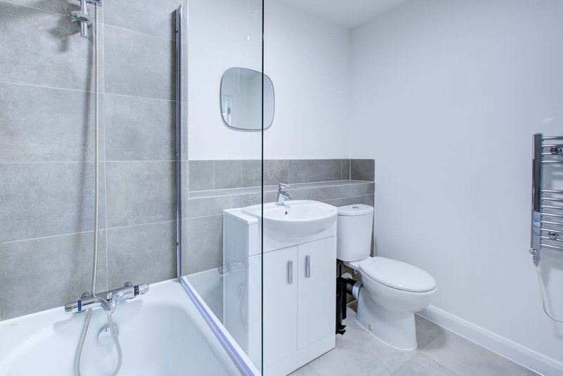 Modern bathroom with white vanity, toilet, bathtub with glass shower enclosure and gray tile