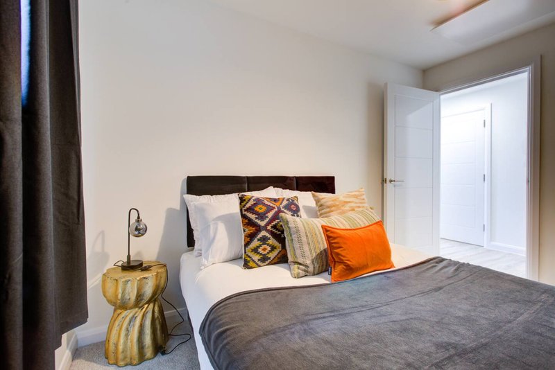 Bedroom with double bed, patterned pillows, orange cushion, gold side table and white door