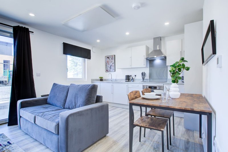 Modern open-plan living room with blue sofa, dining table, and white kitchen units