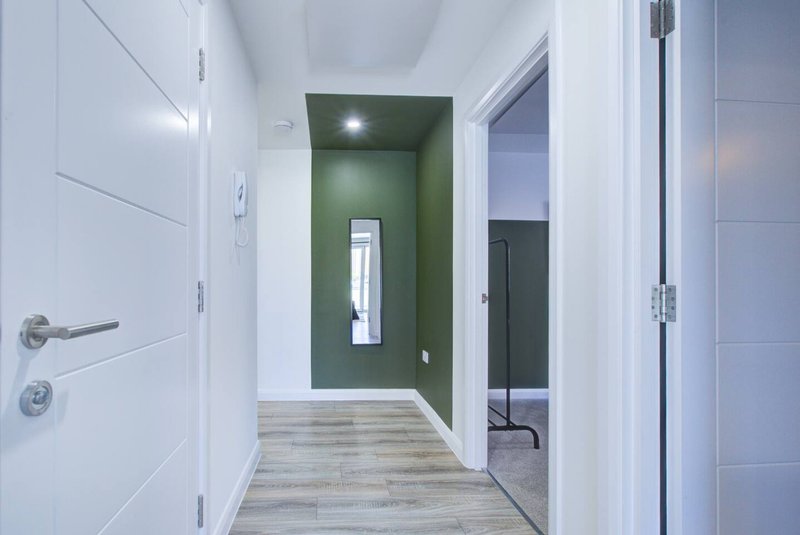 Modern hallway with white doors, green accent wall, wooden flooring and recessed lighting