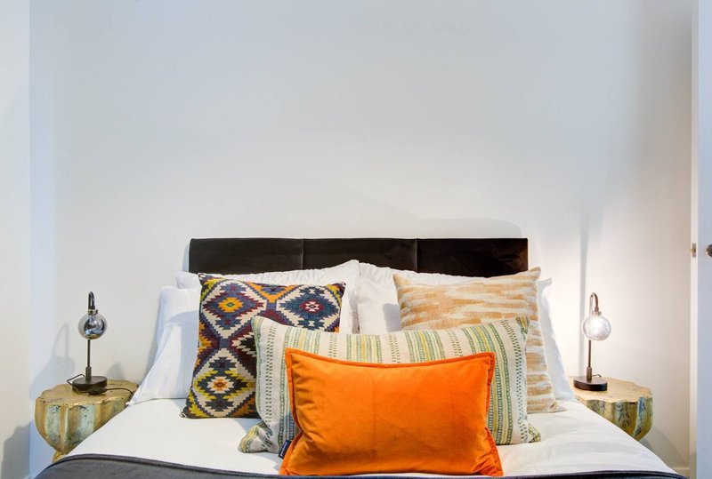 Bedroom with black headboard, white bedding, multiple decorative pillows and orange throw pillow