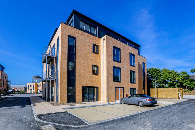 Modern brick apartment building with large windows, ground-floor entrance, and parked car outside