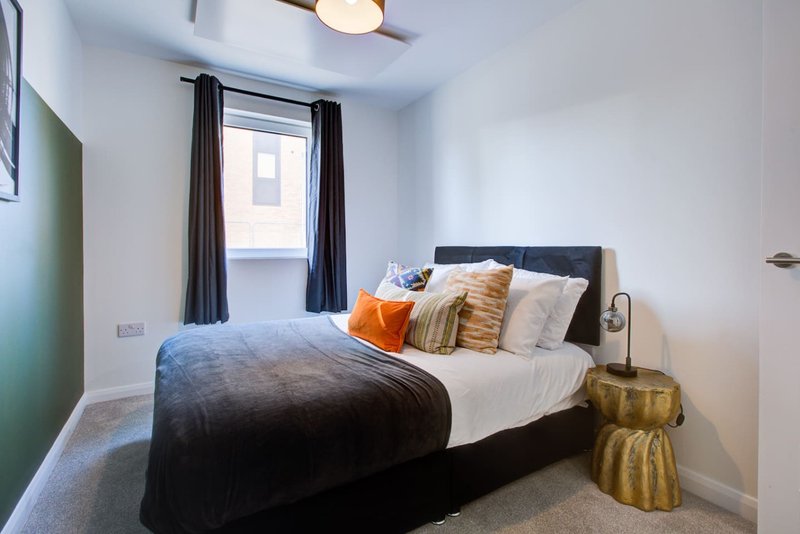 Modern bedroom with double bed, colorful cushions, gold side table and window with black curtains