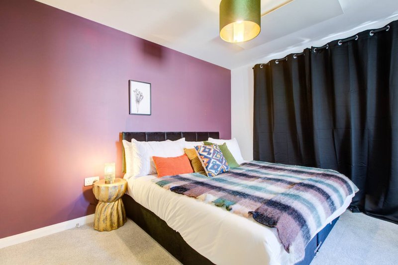 Modern bedroom with purple accent wall, double bed, decorative pillows and striped bedding