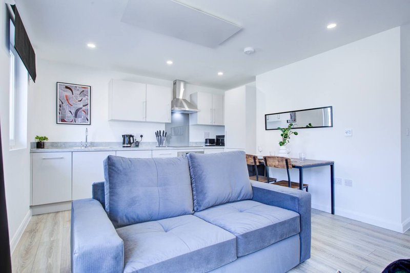 Open-plan kitchen and living area with blue sofa, white cabinetry, and light wooden flooring
