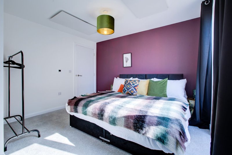 Modern bedroom with double bed, purple accent wall, patterned bedding and green ceiling lamp
