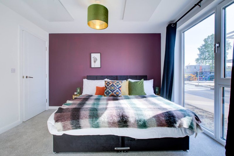 Modern bedroom with purple accent wall, double bed, green pendant light and patio doors