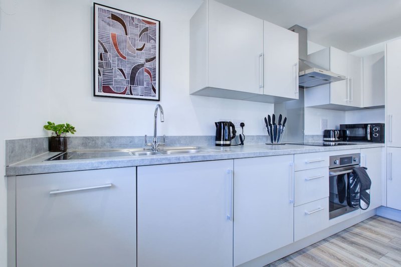 Modern white kitchen with gray countertop, stainless steel appliances and abstract wall art