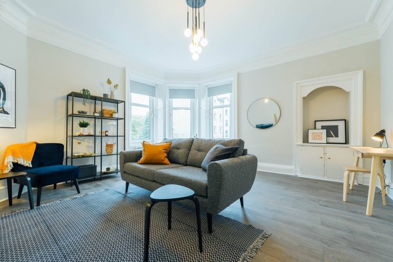 Bright living room with gray sofa, blue armchair, wooden desk, and bay windows