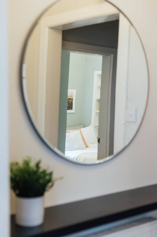 Oval wall mirror above shelf with small potted plant, reflecting bedroom doorway