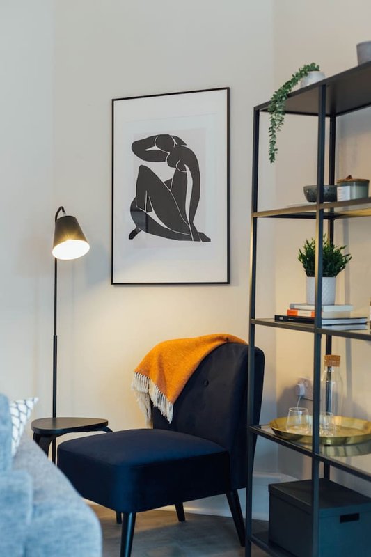 Modern living room corner with navy armchair, floor lamp, framed abstract art and metal shelving unit