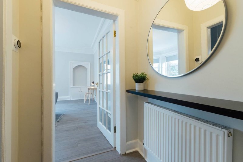 Hallway with cream walls, round mirror, radiator and open doorway to living area