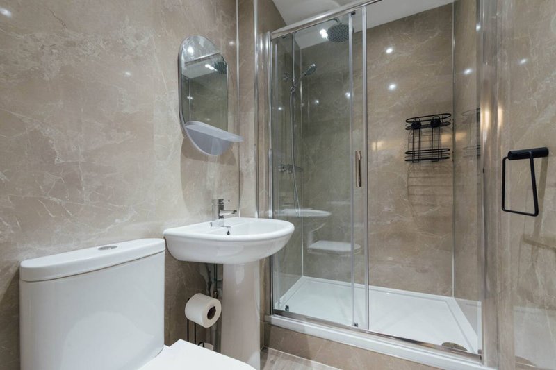 Modern bathroom with toilet, pedestal sink, mirror and enclosed shower enclosure