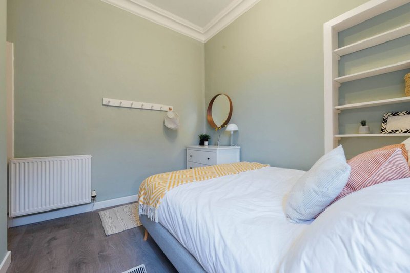Bright bedroom with double bed, white bedding, pink cushions, built-in shelving, and radiator