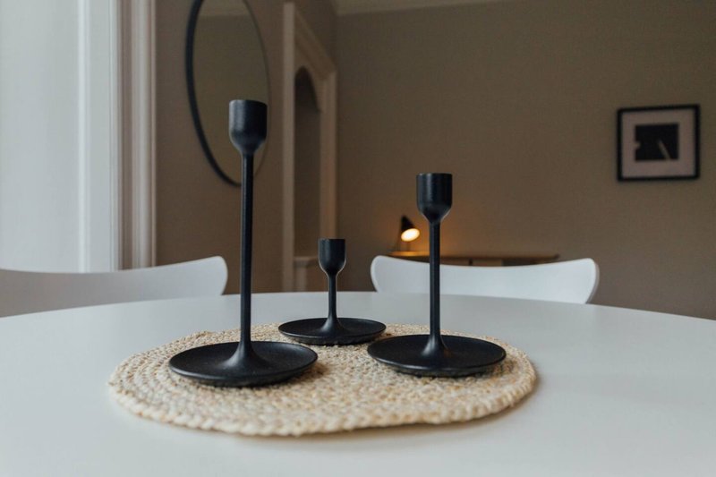 Dining table with white chairs, black candle holders on woven placemat, wall art