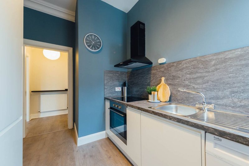 Modern kitchen with blue walls, white cabinetry, stainless steel countertop and black cooker hood
