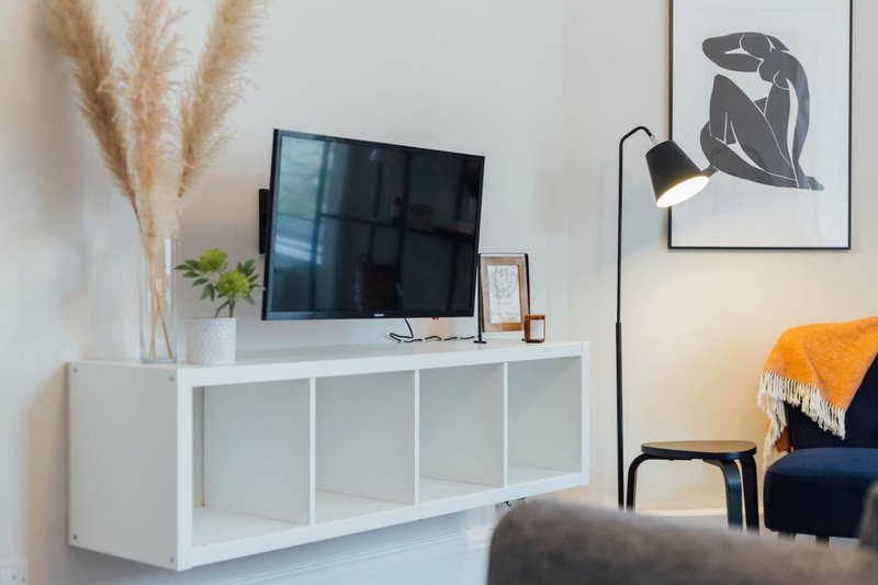 Modern living room with white TV unit, mounted television, wall art and orange throw blanket