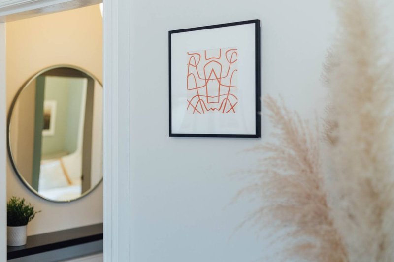 Hallway with round mirror, framed abstract line art, and dried pampas grass decoration